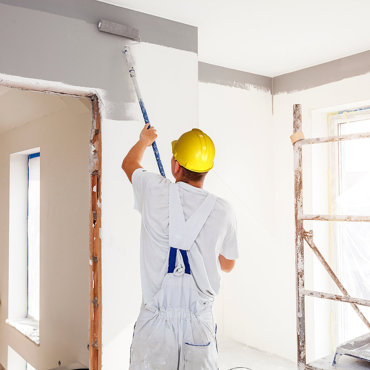 House painter paints a wall in a new home. Unrecognizable Person. Handwerker trägt Farbe auf Bürowand auf - präzise und staubarm