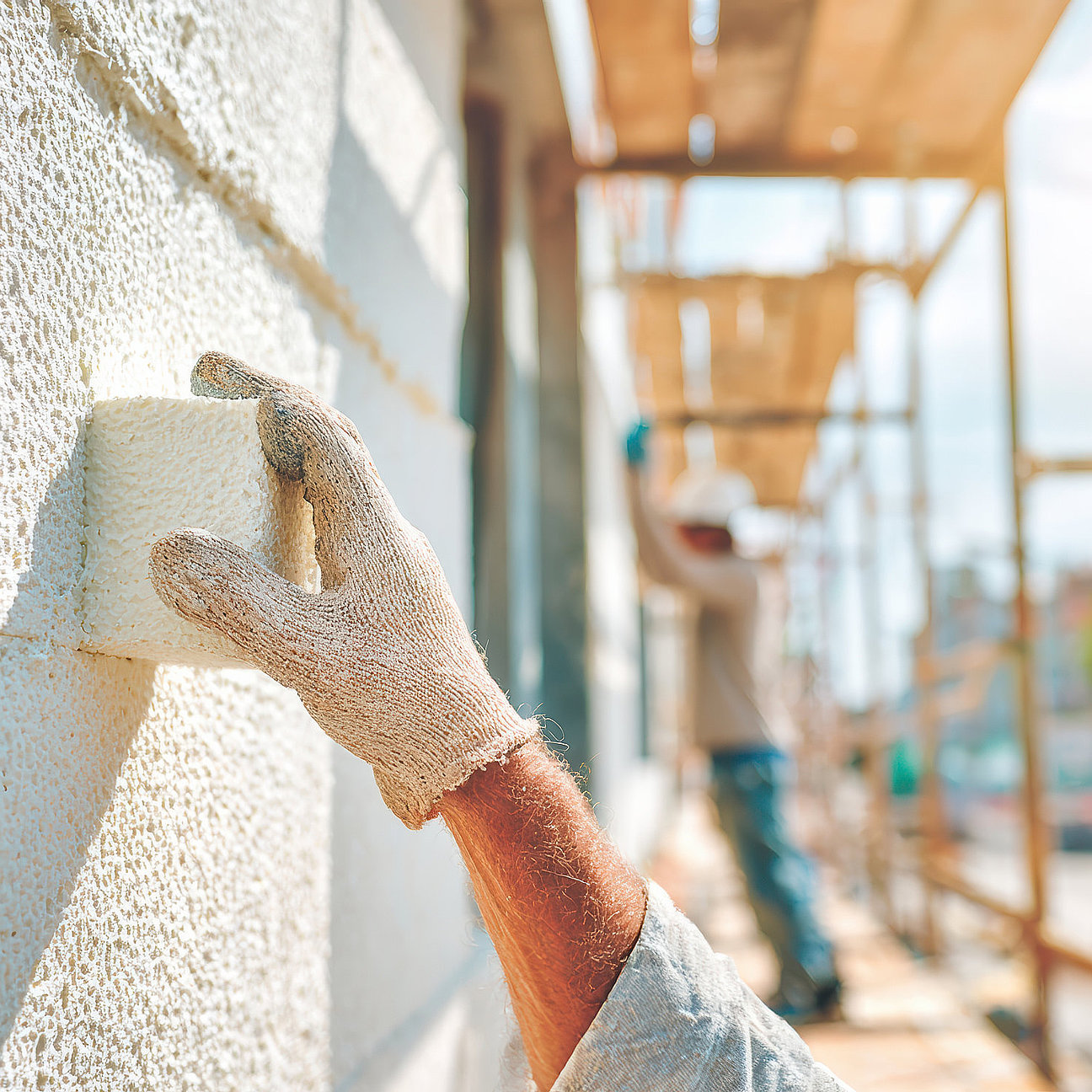 Focused worker on scaffolding during construction renovation installs foam insulation on an exterior wall of building for thermal efficiency Handwerker auf Gerüst beim Streichen der Fassade - präzise Ausführung