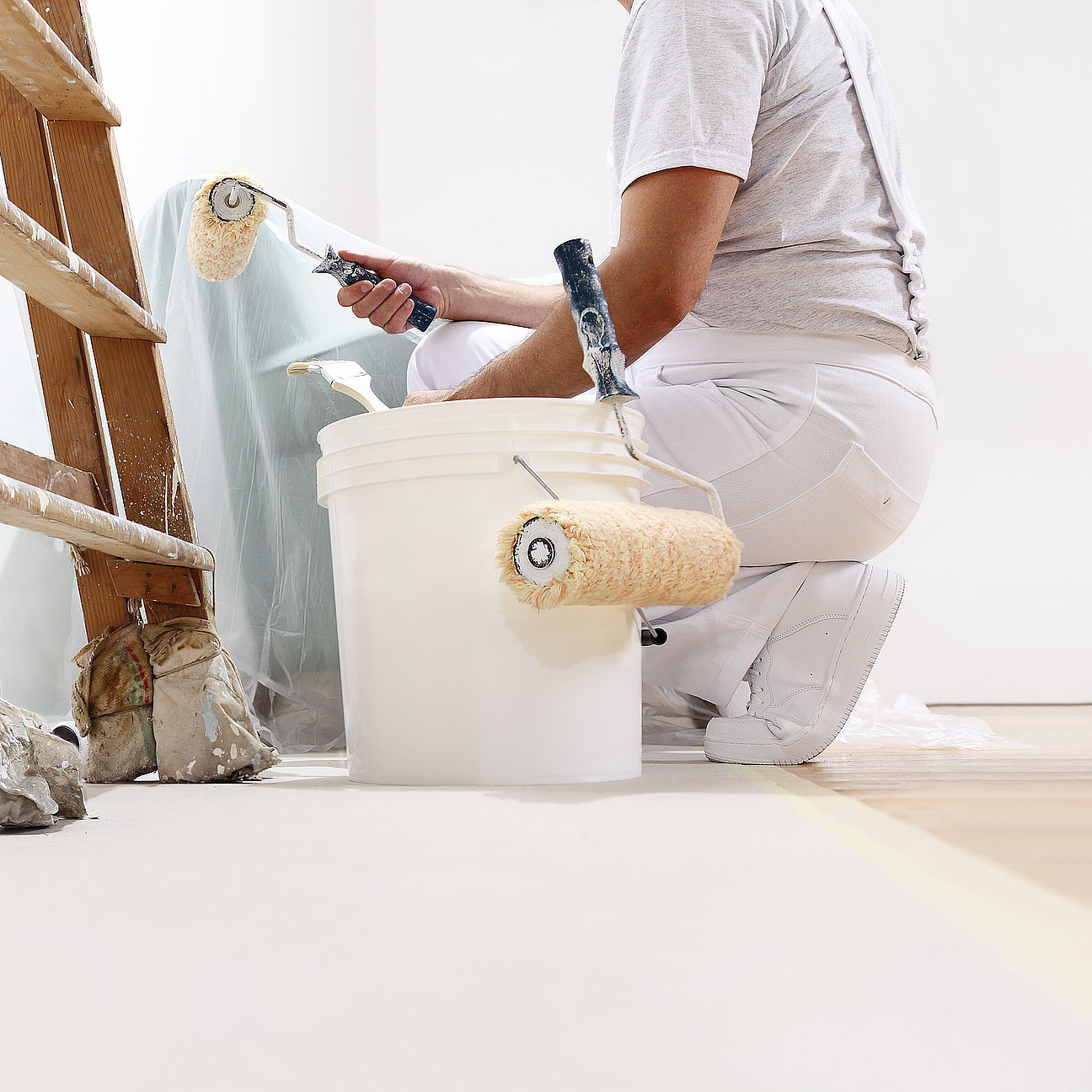 painter man at work with a roller, bucket and scale, from below Fachmann auf Gerüst beim Beschichten einer Fassade
