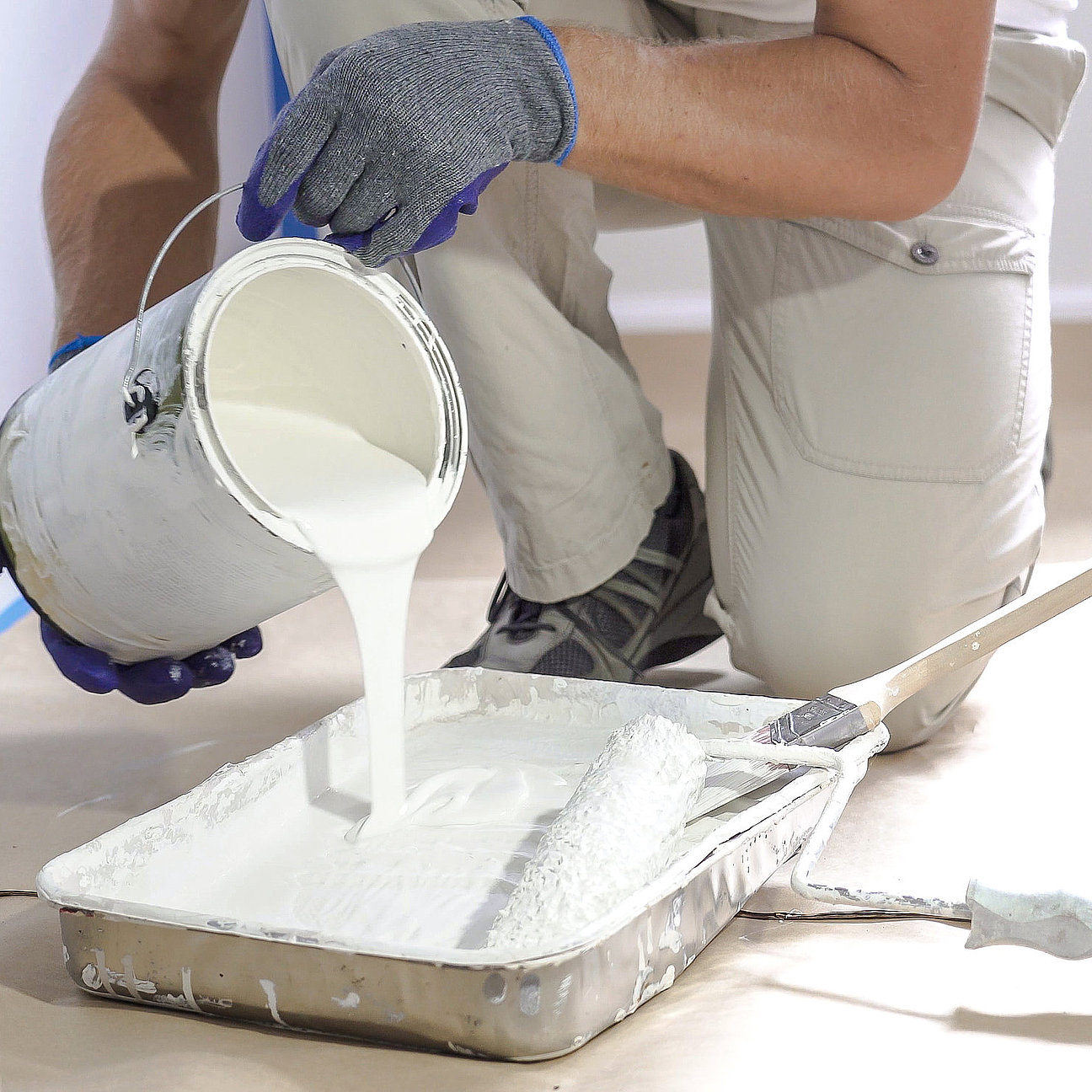 Professional interior construction worker pouring white color paint to tray. Farbkonzept für Büro - harmonische Kombination aus Neutral- und Akzentfarben
