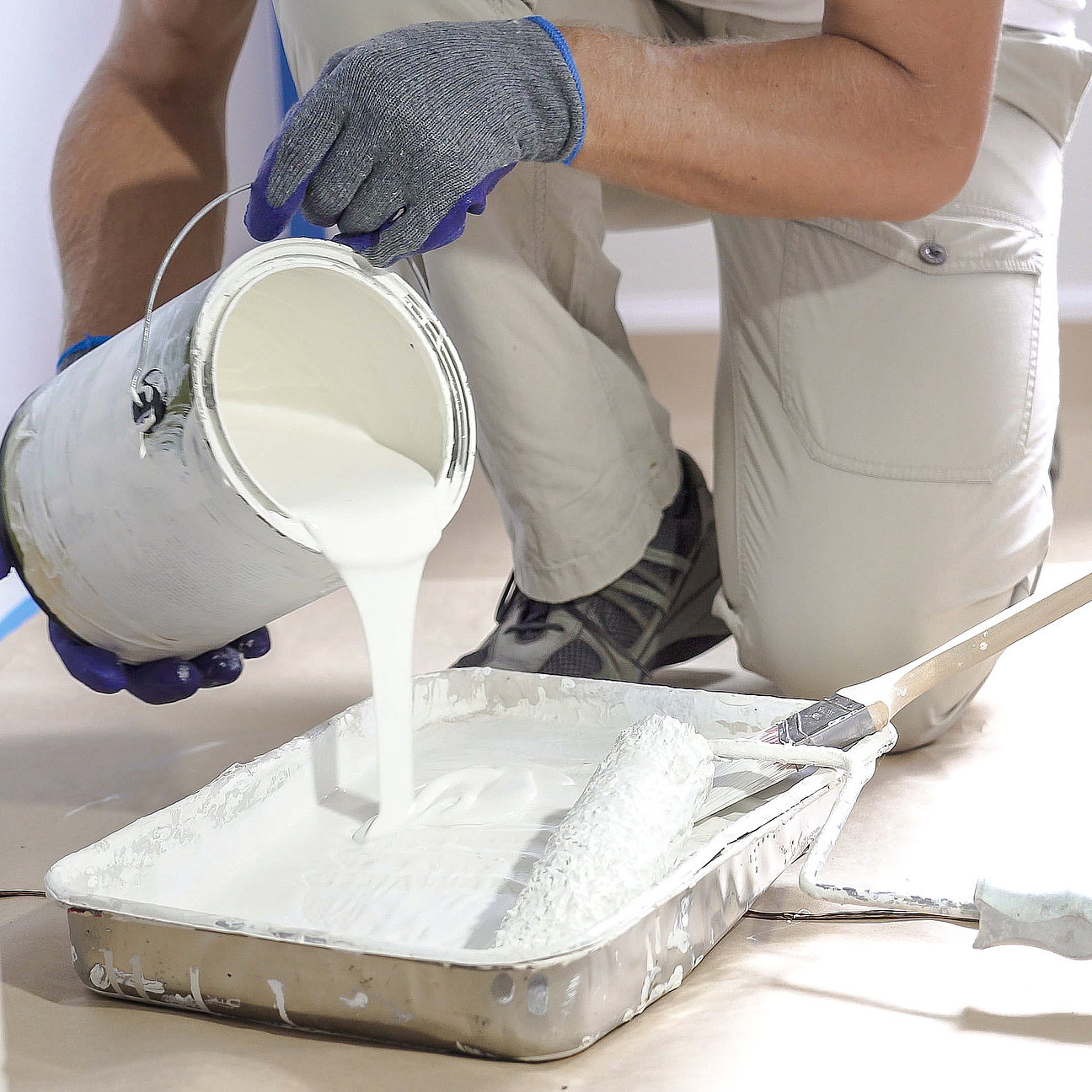Professional interior construction worker pouring white color paint to tray. Hochwertiger Fassadenanstrich für Einfamilienhaus - langlebiger Wetterschutz