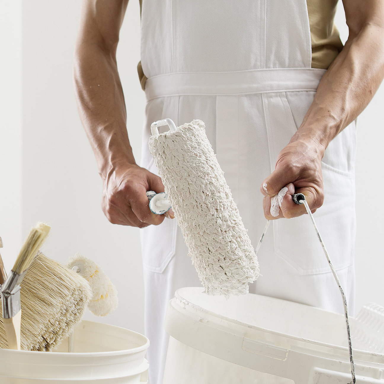 hands of house painter man decorator work of home to renovate, using roller paint and holding white bucket, a wooden ladder with paint brushes as background, close-up Malermeister bei Farbberatung im Wohnraum