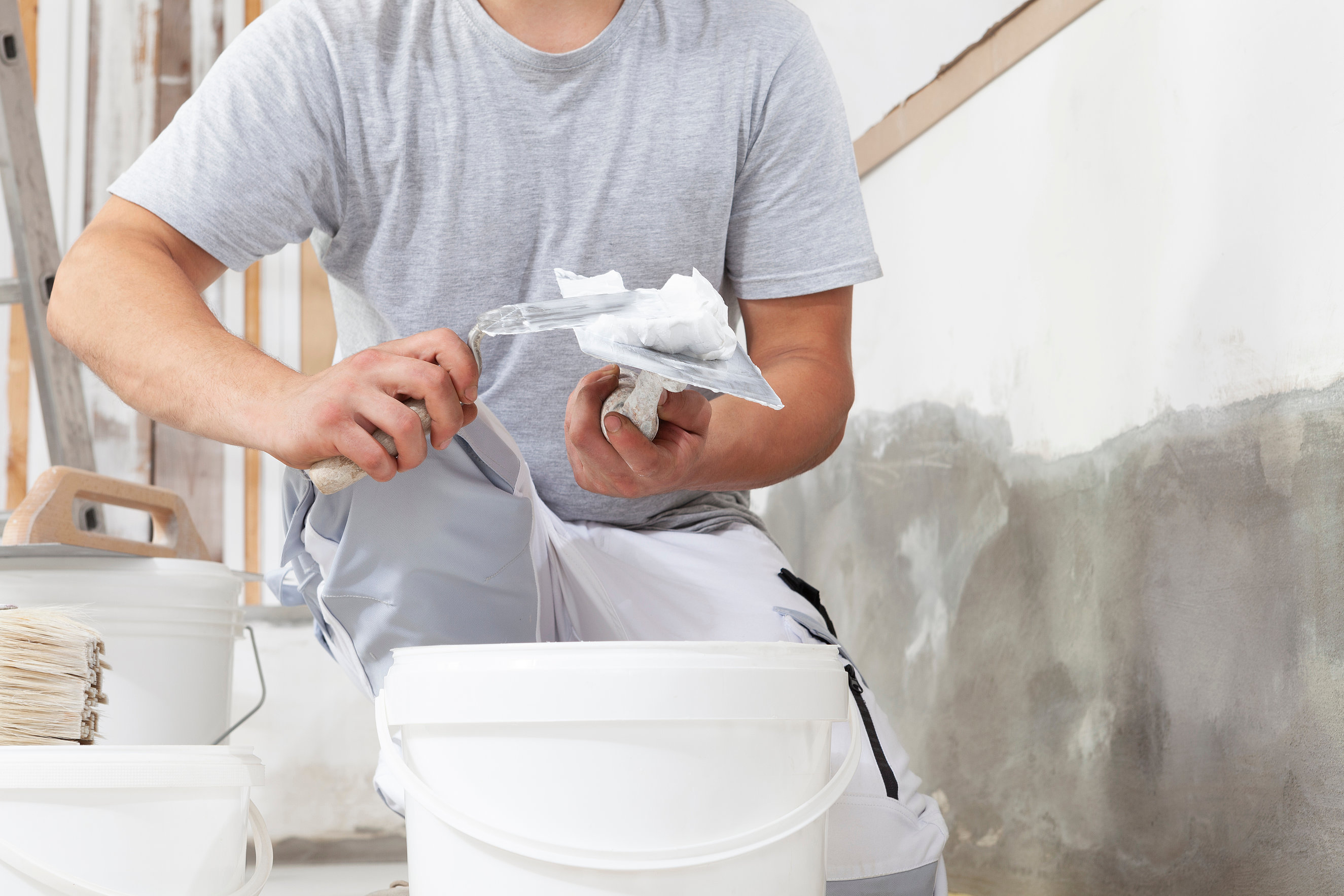 Hands man plasterer construction worker at work closeup, takes plaster from bucket and puts it on trowel to plaster the wall, inside the building site of a house Professionelle Verputzarbeiten an Fassade und Innenwand - Crössmann Baudekoration
