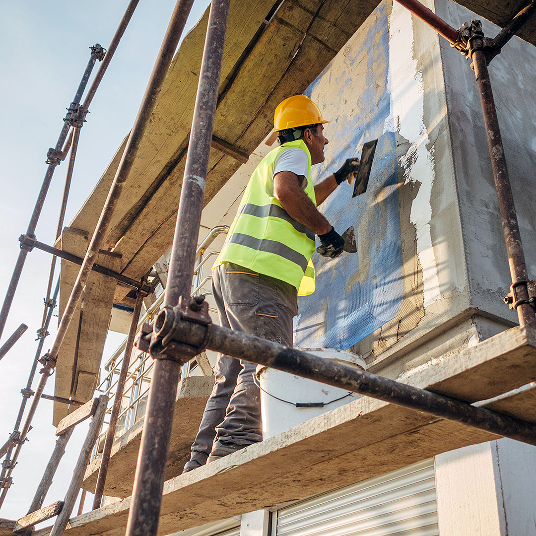 Fassade für die energetischen Sanierung Ein Bauarbeiter steht auf einem Gerüst und bereitet eine Fassade für die energetischen Sanierung vor.