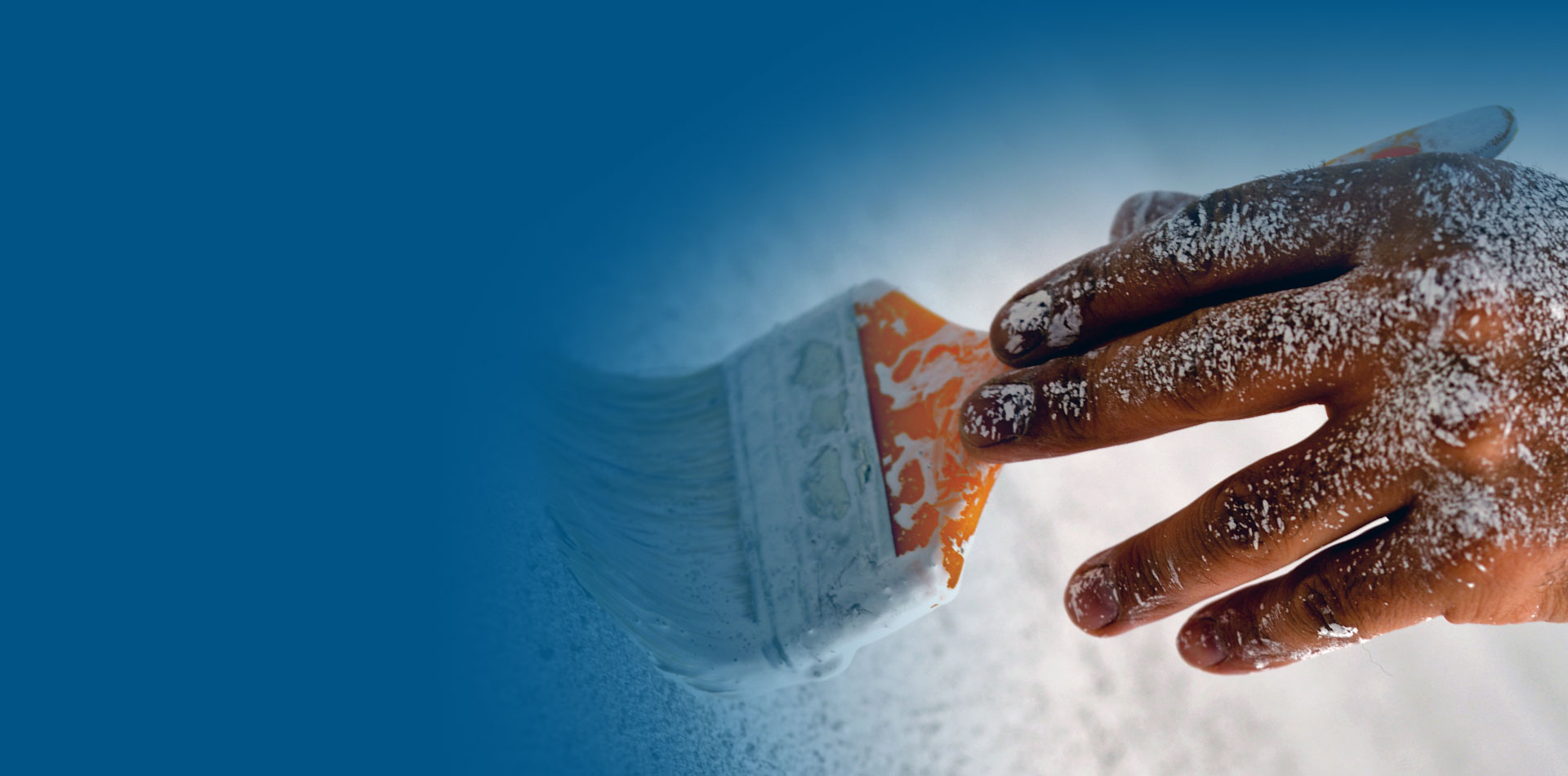 Nahaufnahme einer Renovierung: eine Hand führt einen Pinsel mit weißer Wandfarbe.